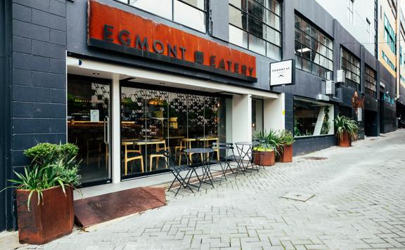 The exterior of Egmont St Eatery, chairs sit outside and the brick walls are painted black.