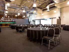Chairs around circle tables inside a large function centre.