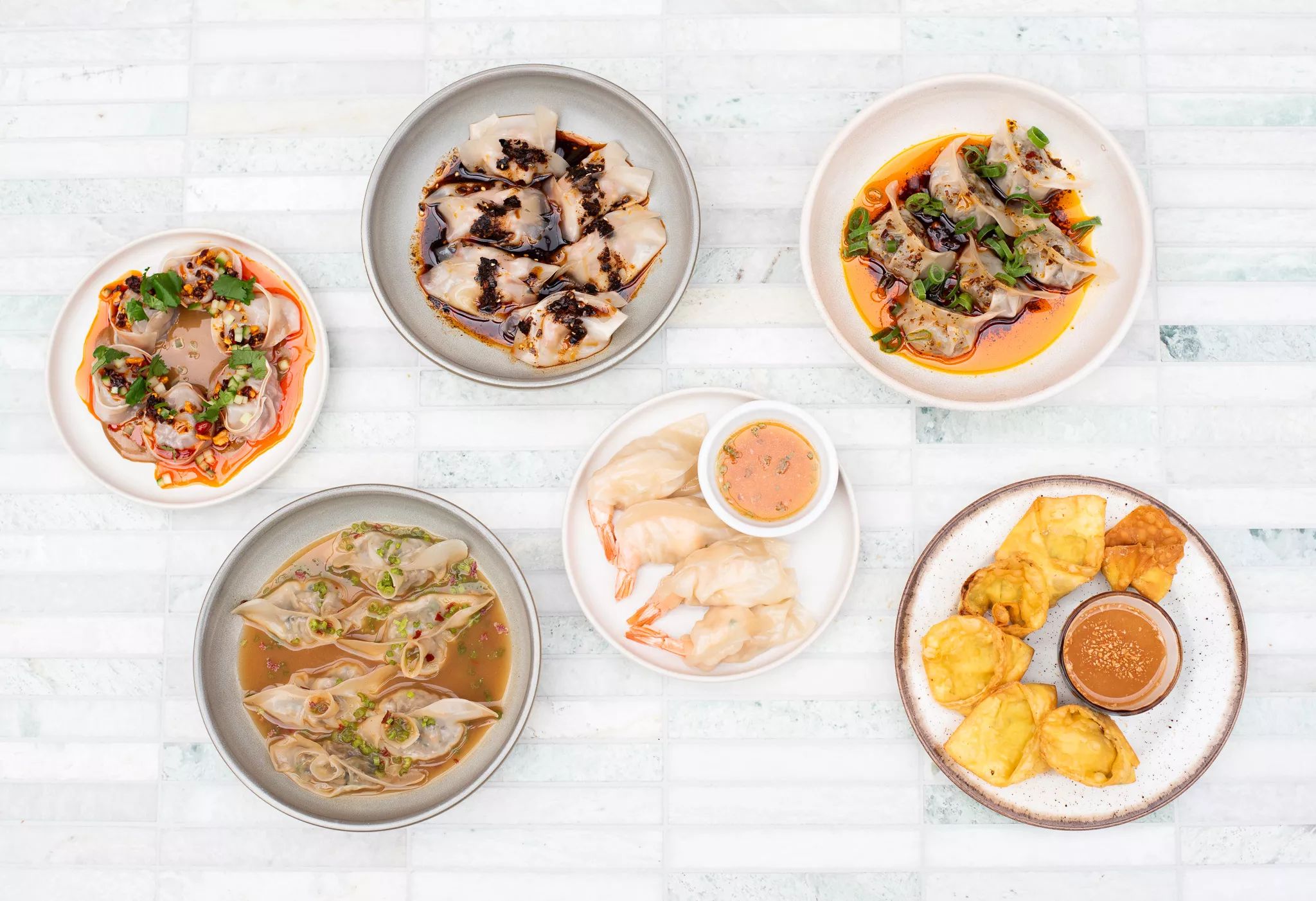 Aerial shot of six plates of food on a white tiled table.