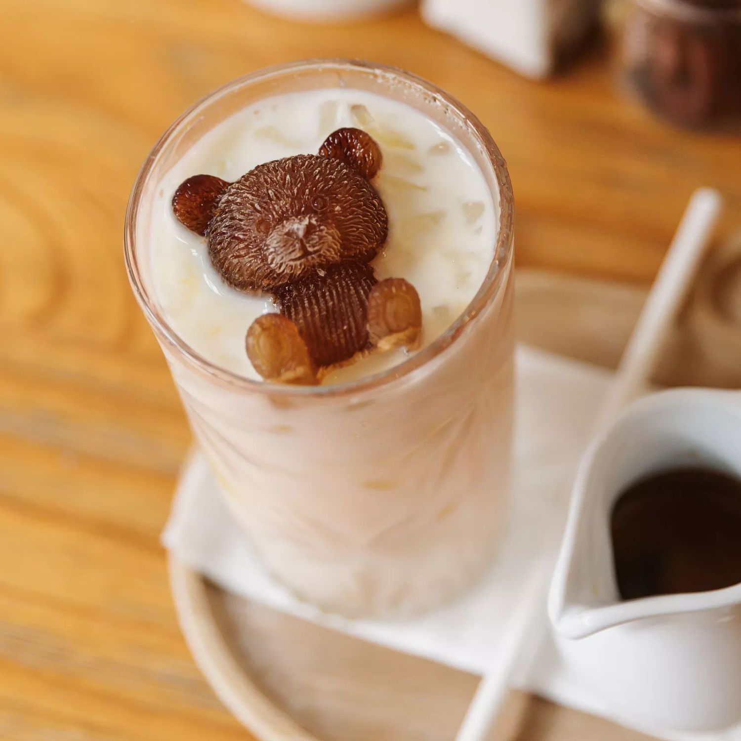 Looking down on an iced coffee made by Gemini Cafe & Eatery, a glass of iced milk with a chocolate bear sits to the left and a little shot of espresso next to it.