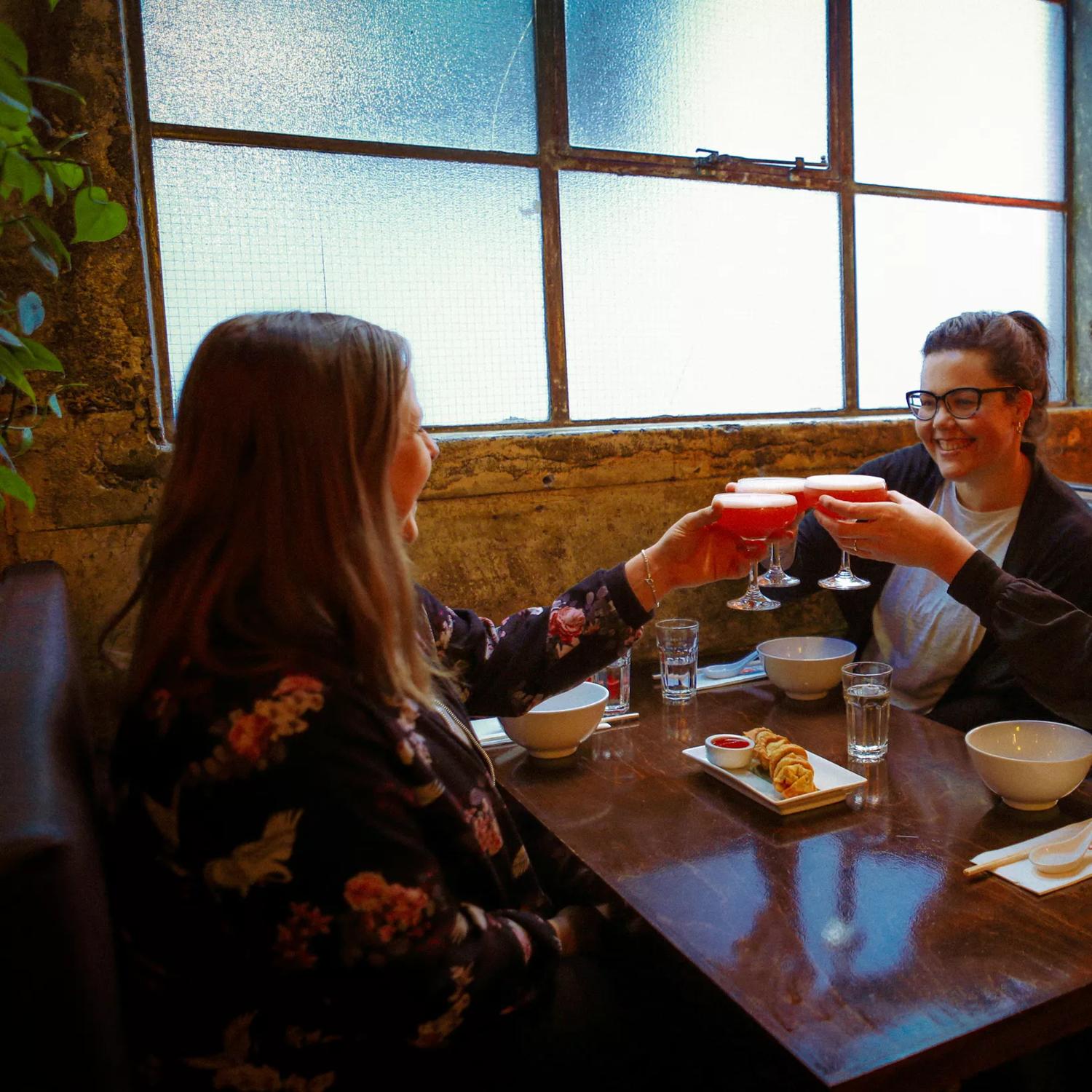 Three friends sit in a booth, enjoying an appetizer and cocktails at Chow, an Asian restaurant in Te Aro Wellington.