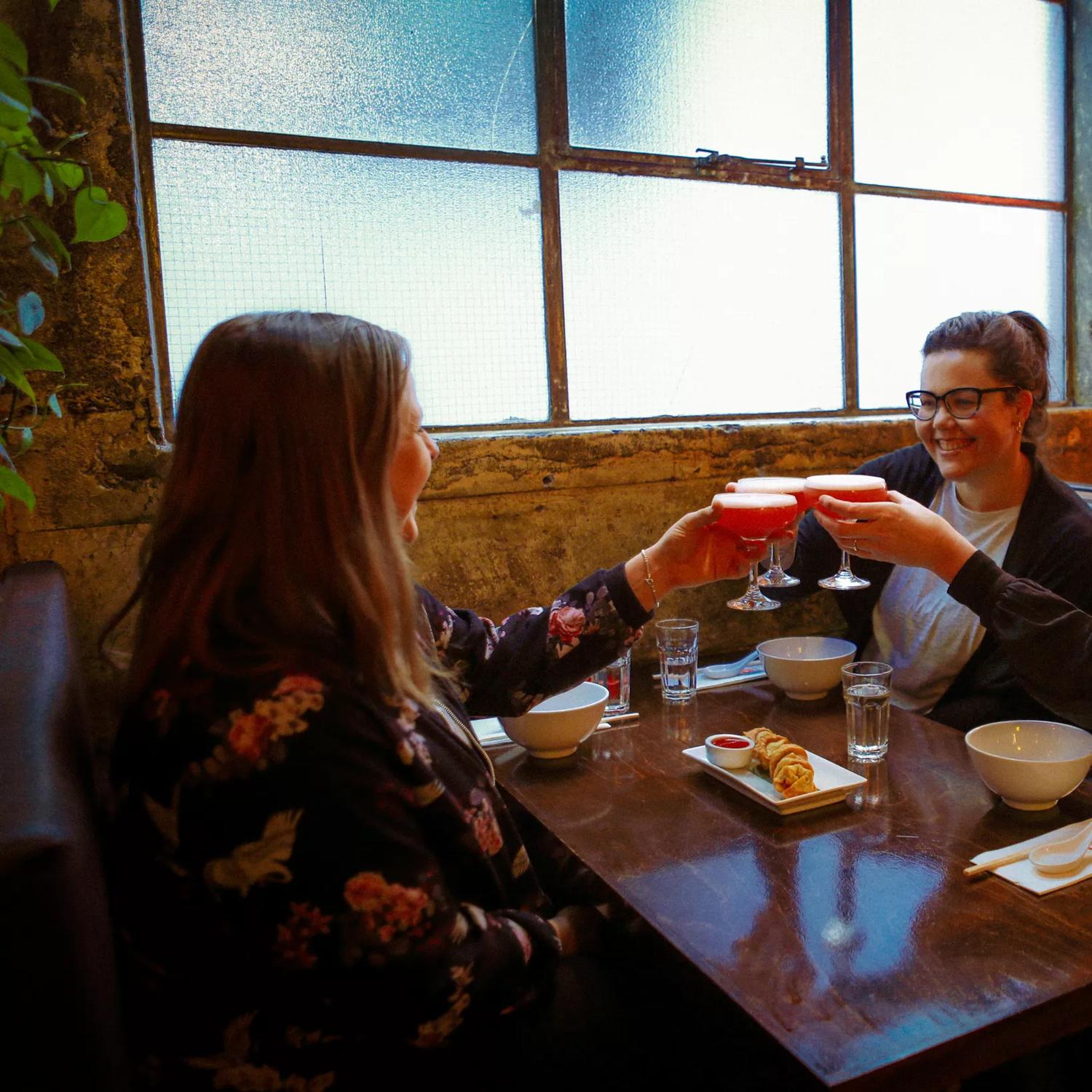 Three friends sit in a booth, enjoying an appetizer and cocktails at Chow, an Asian restaurant in Te Aro Wellington. 