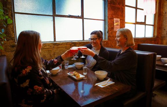 Three friends sit in a booth, enjoying an appetizer and cocktails at Chow, an Asian restaurant in Te Aro Wellington. 