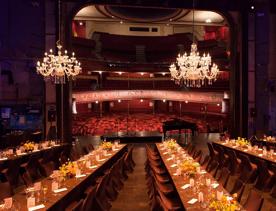 the stage of The Opera House set up for a private function with long tables and chairs with chandeliers hanging above.