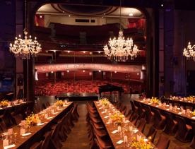 the stage of The Opera House set up for a private function with long tables and chairs with chandeliers hanging above.