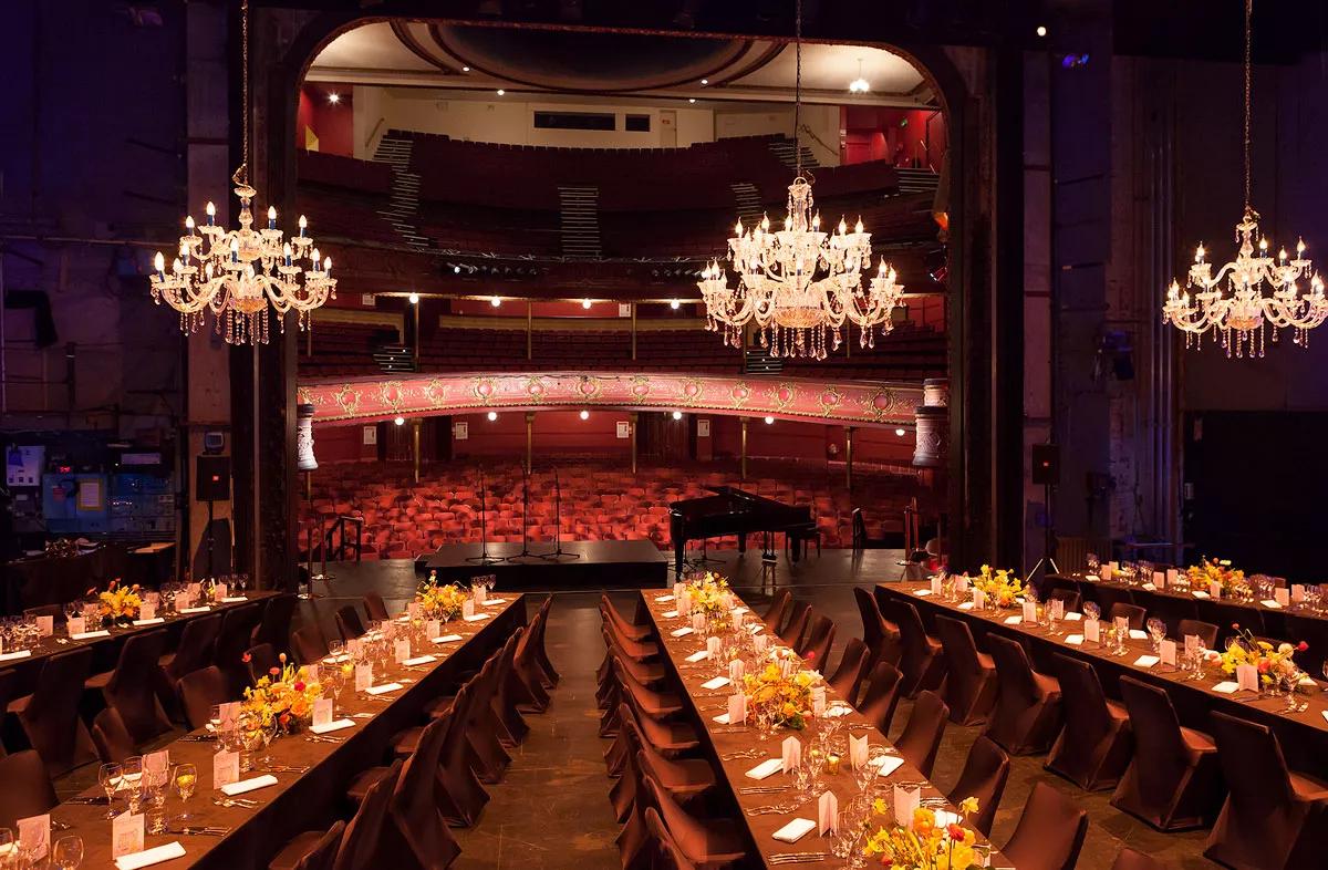 the stage of The Opera House set up for a private function with long tables and chairs with chandeliers hanging above.