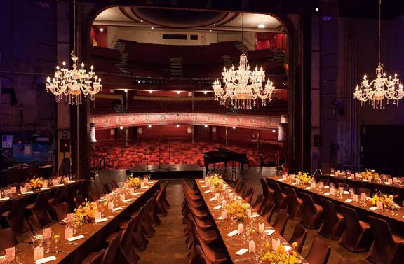 the stage of The Opera House set up for a private function with long tables and chairs with chandeliers hanging above.