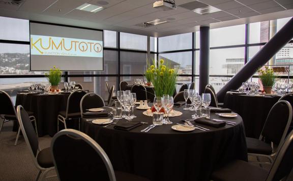 A conference room with four round tables set up with dinner-wear and floral centrepieces.