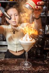 A waiter inside The Library pouring cinnamon on a cokctail and lighting it with a torch lighter.