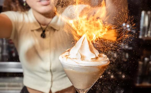 A waiter inside The Library pouring cinnamon on a cokctail and lighting it with a torch lighter.