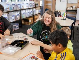 3 children and an adult sit at table at House of Science and play with magnets.