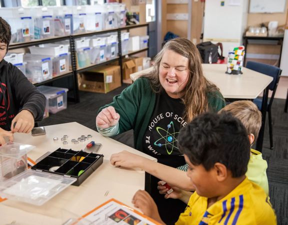 3 children and an adult sit at table at House of Science and play with magnets.