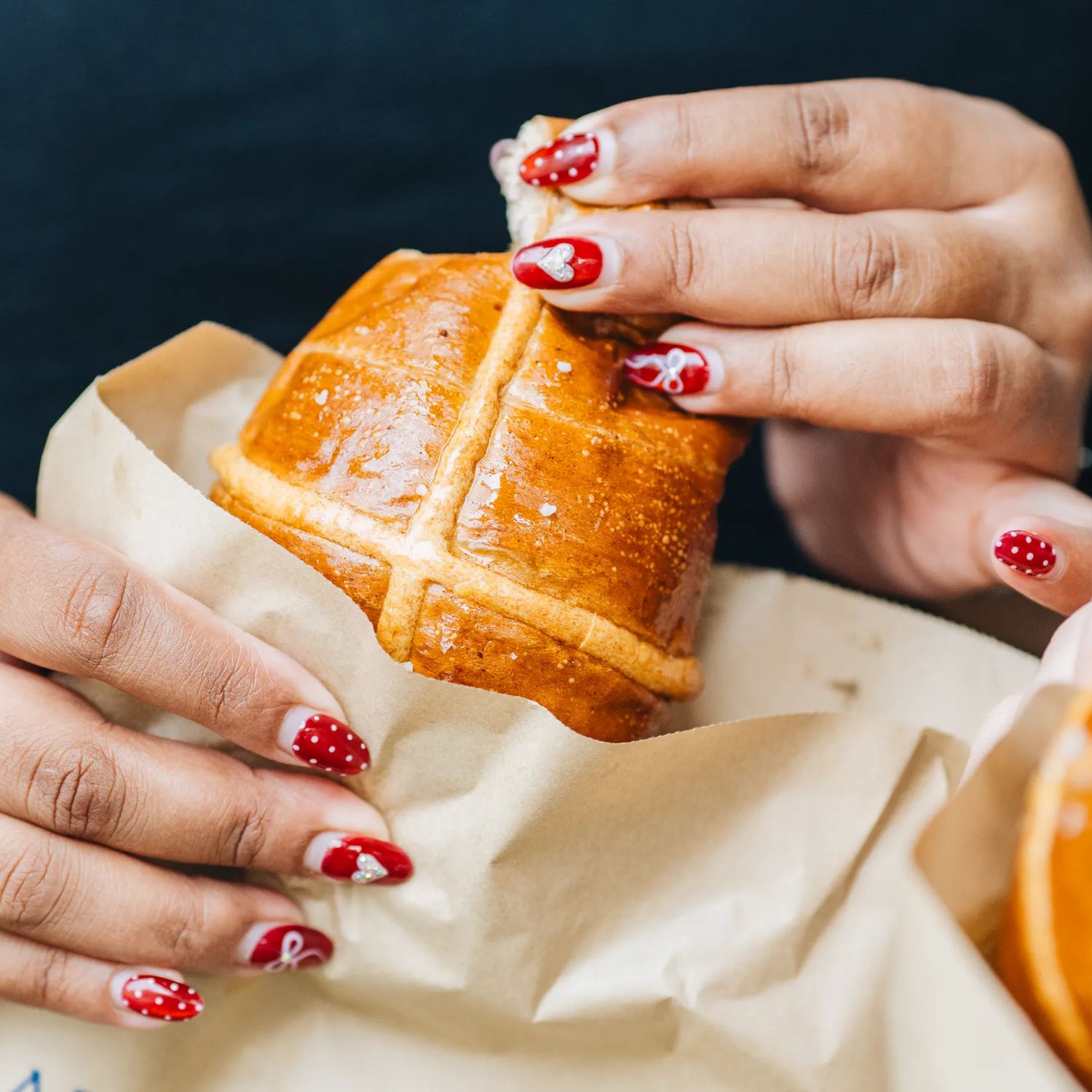 A person tears a piece off a hot cross bun.