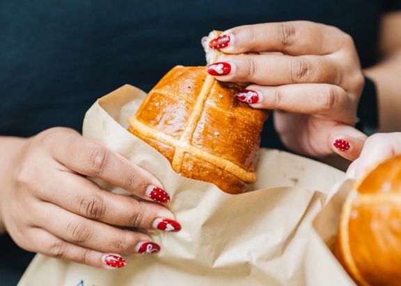 A person tears a piece off a hot cross bun.