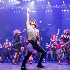 A scene from We Will Rock You, the blockbuster Queen musical with sixteen performers dancing in punk-rock style costumes.