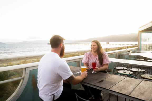 Two people enjoying drinks on the patio of Seashore Cabaret, a café and restaurant located on the Esplanade in Petone, Lower Hutt. 