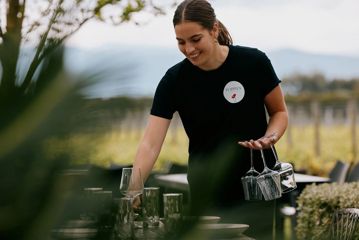 Person holding empty glasses at Poppies with vines in the background