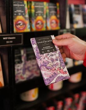 A person holding a purple bar of wrapped chocolate in Wellington Chocolate Factory.