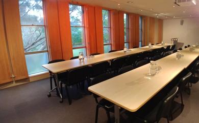 A conference room set up with two long tables, chairs, water pitchers and glasses.