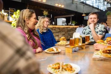 Person laughing with friends whilst sitting at a table with beers and bar food at Aro Bar in Brewtown, Upper Hutt.