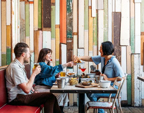 Three people eat crab and other seafood plates at The Crab Shack on Queens Wharf.