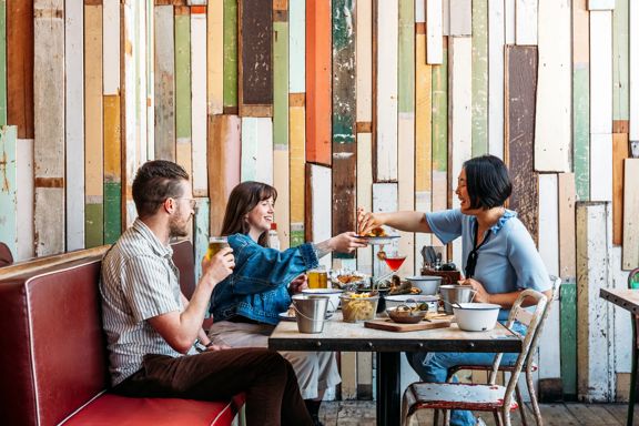 Three people eat crab and other seafood plates at The Crab Shack on Queens Wharf.