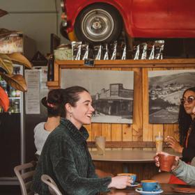 Two people chatting inside The Big Salami in Porirua. A giant red car sits on the wall as decoration.