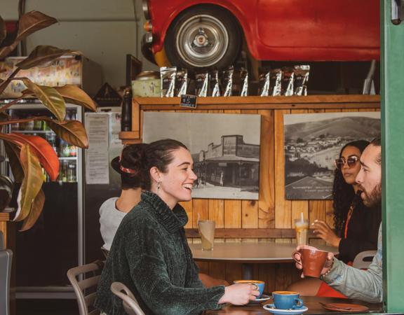 Two people chatting inside The Big Salami in Porirua. A giant red car sits on the wall as decoration.