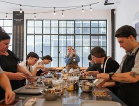 A group of six people on the Chocolatier experience at Wellington Chocolate Factory. They are all scooping toppings from a jar onto chocolate.