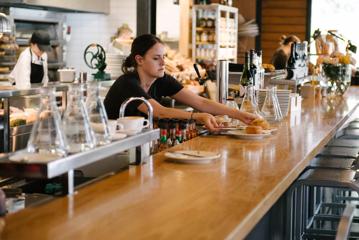 A worker placing plates of food onto a counter at Prefab Eatery.