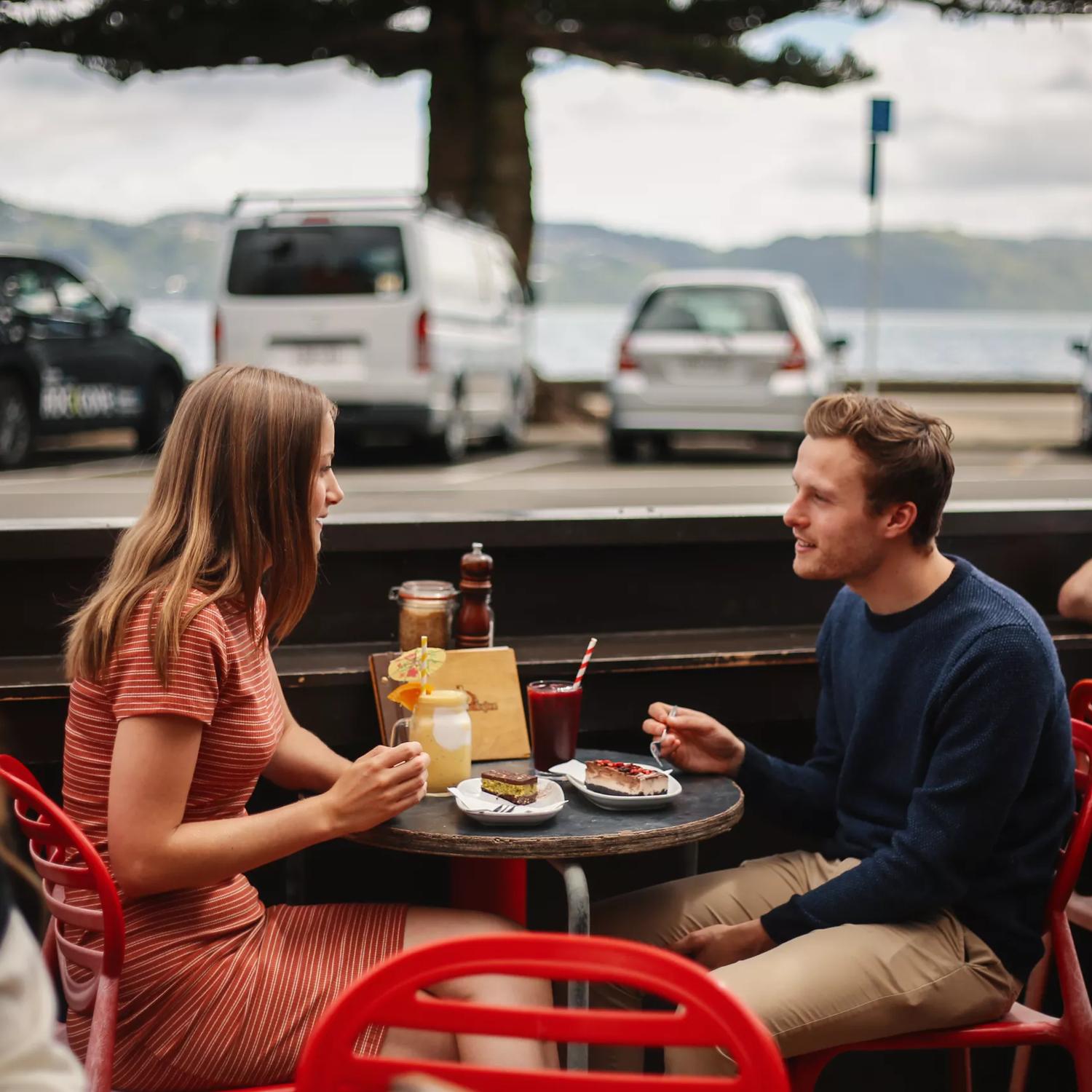 2 people enjoying food and drinks at an outside table at Beach Babylon, across the road from Oriental bay.