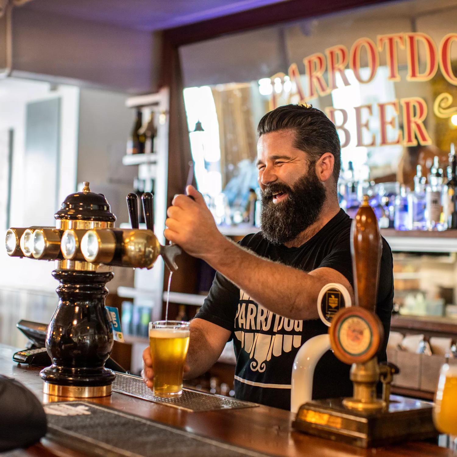 The bar staff at Parrotdog pouring a drink while laughing with a customer.