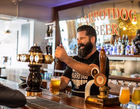 The bar staff at Parrotdog pouring a drink while laughing with a customer.