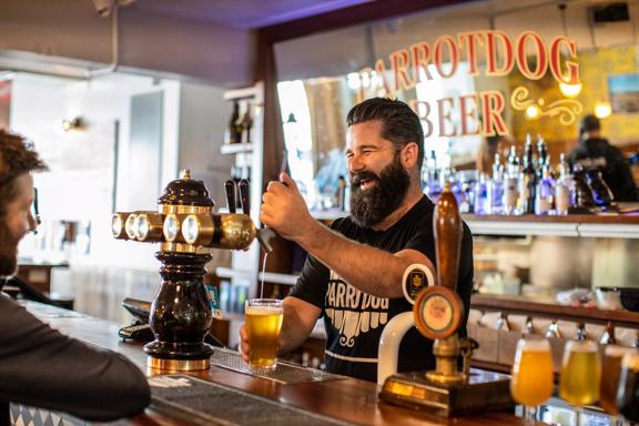 The bar staff at Parrotdog pouring a drink while laughing with a customer.