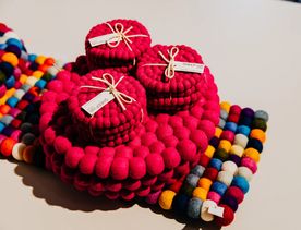 Handcrafted pink felt ball tableware accessories displayed alongside a colourful striped felt table runner.