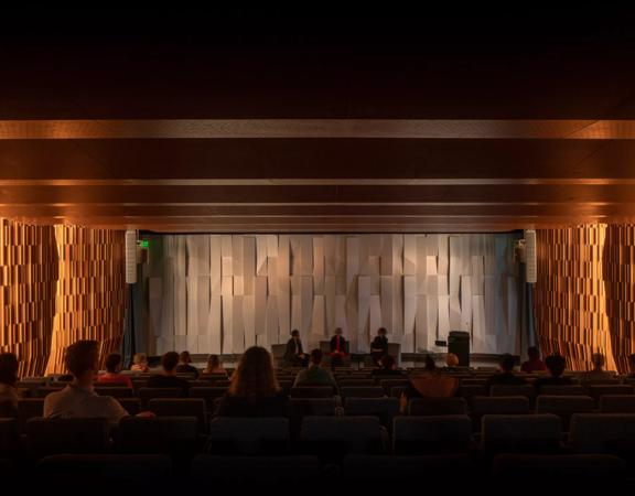 Tiakiwai conference centre auditorium view showing rows of seating and a stage with three people on chairs.