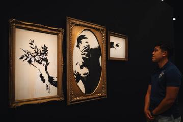 A person looks at The Flower Bomber tryptic at THe Art of Banksy Exhibition.