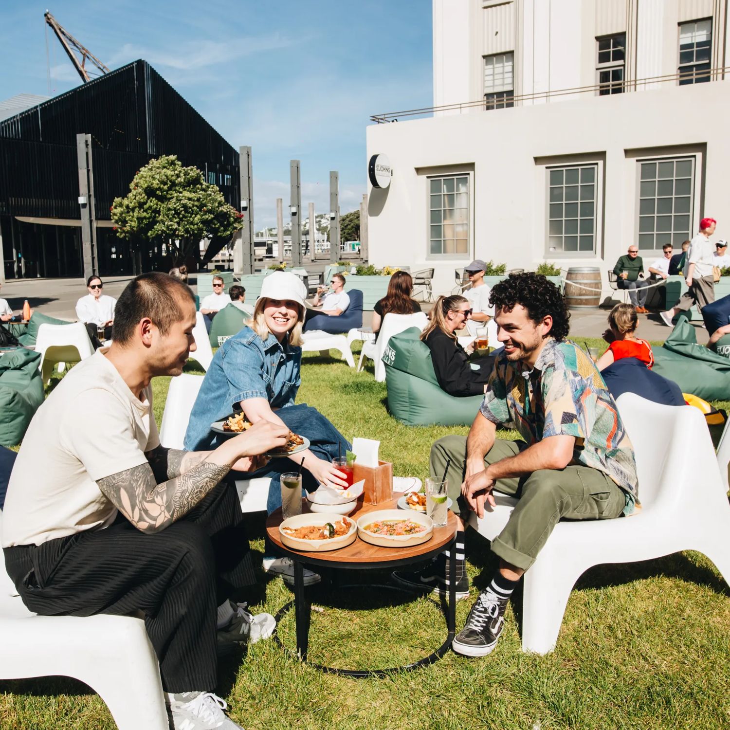 Three people enjoying food and drinks outside on the grass at St John's bar on a sunny day