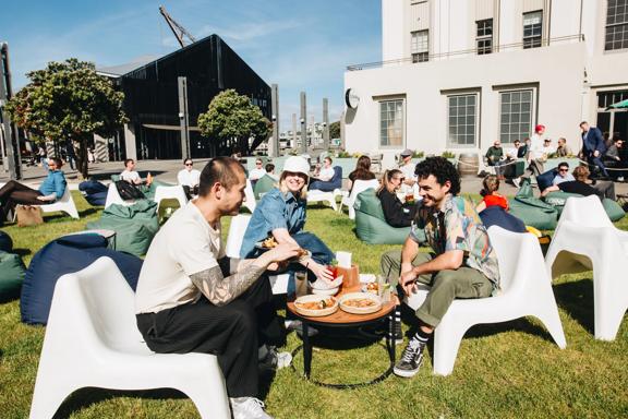 Three people enjoying food and drinks outside on the grass at St John's bar on a sunny day