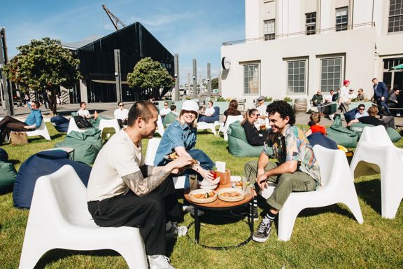 Three people enjoying food and drinks outside on the grass at St John's bar on a sunny day