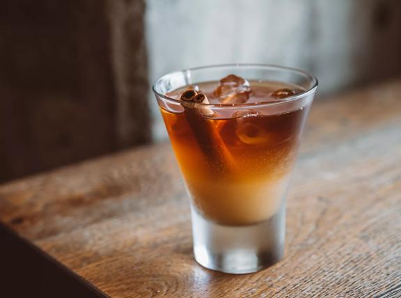 A shot of espresso made by New Chapter, in a shot glass with cinamon sticks inside.