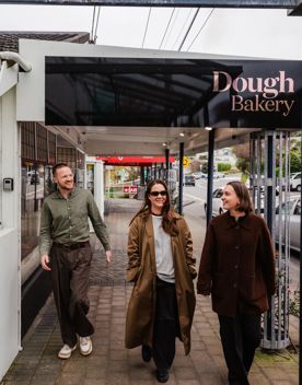 Three people walk past Dough Bakery in Wellington, with the bakery entrance and street frontage visible in the background.