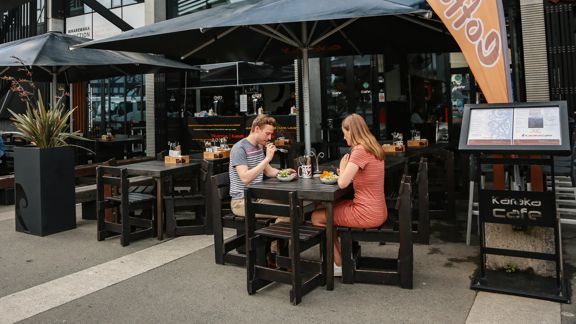 2 customers seated at outside tables at Karaka Cafe at Te Wharewaka o Pōneke.