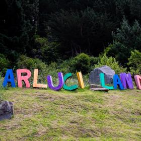 On a hill the sign for Carlucci Land sits among large rocks. It is made of corrugated iron and painted in different colours.