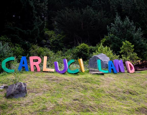 On a hill the sign for Carlucci Land sits among large rocks. It is made of corrugated iron and painted in different colours.