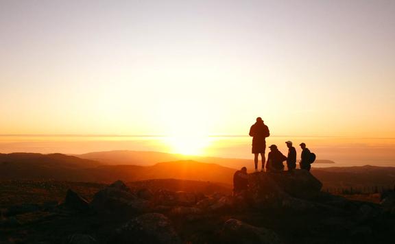 Five people standing on the summit of Boulder Hill, Puke Ariki in Belmont Regional Park at sunset.