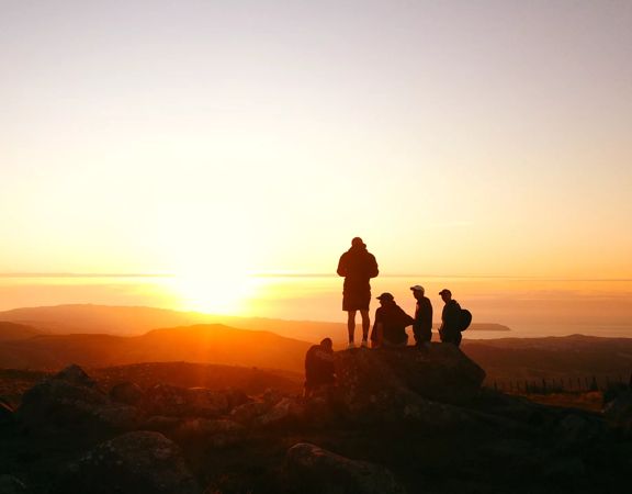 Five people standing on the summit of Boulder Hill, Puke Ariki in Belmont Regional Park at sunset.