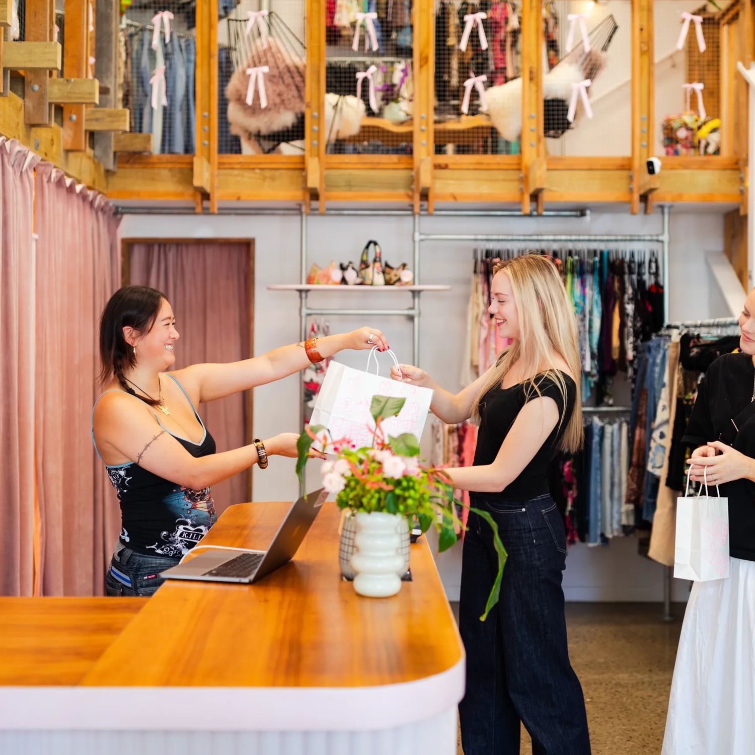 Person handing a garment to a customer at the counter inside Preloved Charlies.