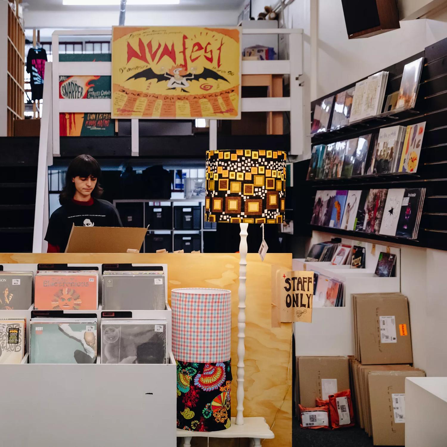 The interior of Flying Nun, a record store located on Cuba Street in Te Aro, Wellington. A worker is standing behind the counter surrounded by vinyl records. 