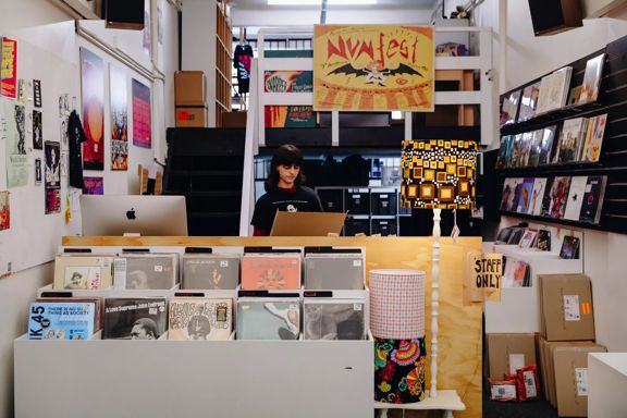 The interior of Flying Nun, a record store located on Cuba Street in Te Aro, Wellington. A worker is standing behind the counter surrounded by vinyl records.